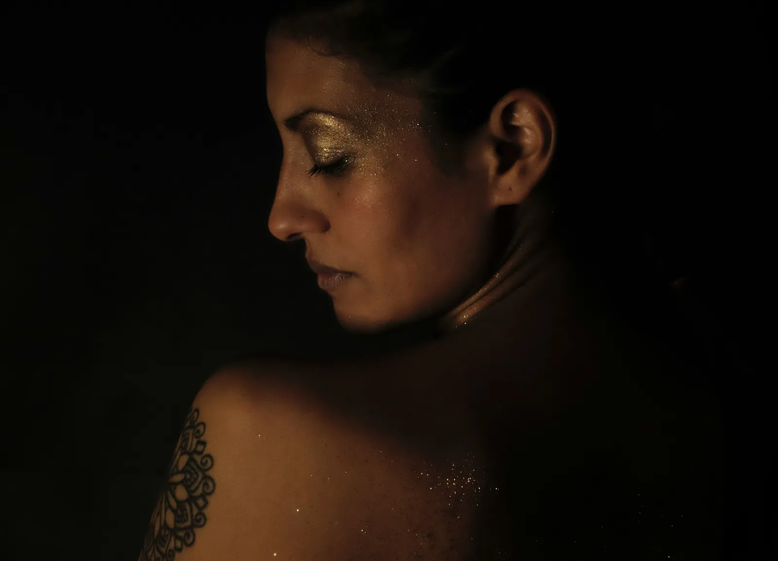 Mujer en penumbra con luz cálida sobre el hombro
